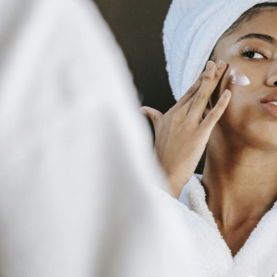 Ethnic woman applying cream on face in morning
