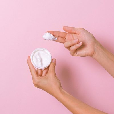 Unrecognizable person with can of moisturizing cosmetic cream for daily routine in hands on pink background in studio during procedure